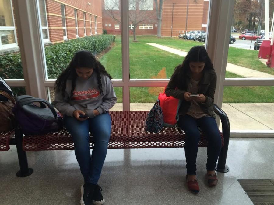 Two+AHS+students+use+their+phones+in+the+front+office.