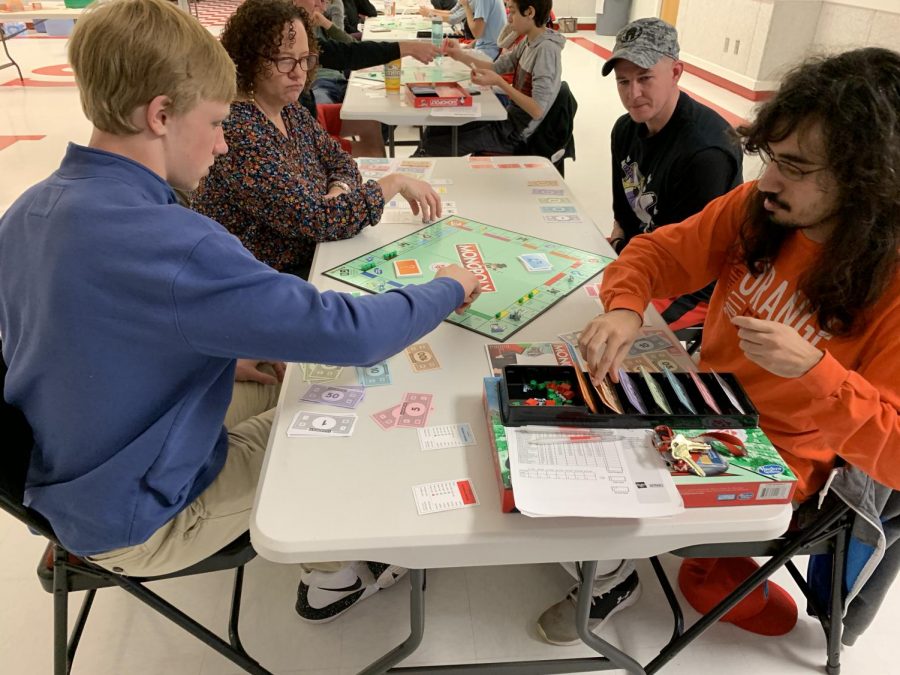 Senior Alex Bellem (left) moves his piece on the Monopoly board after a turn and Math teacher Evaristo Martins (Right) deals money as the broker for the first round of the day at the Monopoly tournament. 