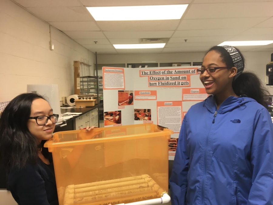 Sophomores Han Le and Haleluya Worku practice presenting for the science fair. Le is pictured holding the fluidized bed from her project.